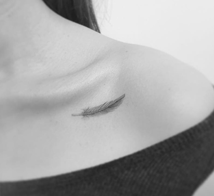 Minimalist feather tattoo on collarbone by a Korean artist.