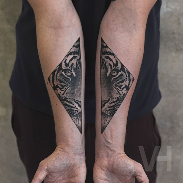 Symmetrical tattoos of a tiger's face on forearms, blending nature and geometry by Valentin Hirsch.