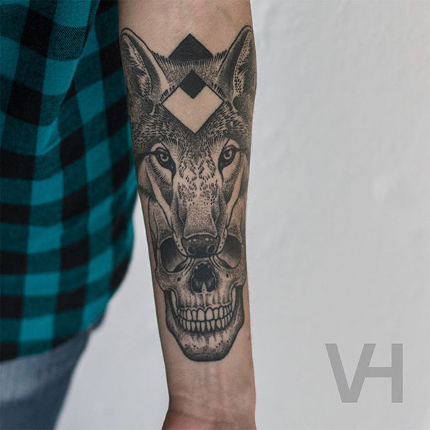 Symmetrical tattoo by Valentin Hirsch on forearm, combining a wolf's head and skull with geometric patterns.