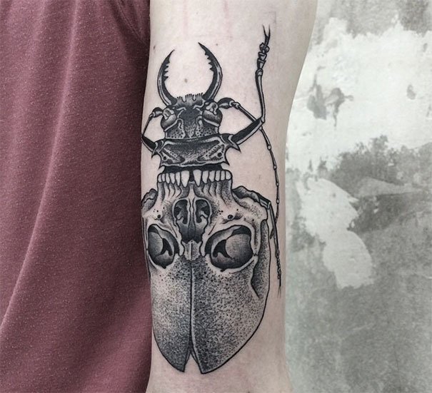 Symmetrical tattoo on arm by Valentin Hirsch, featuring a beetle and skull design blending nature and geometry.