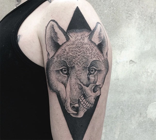 Symmetrical tattoo of a wolf merging with a skull, designed with geometric elements on an upper arm.