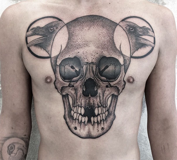 Symmetrical tattoo of a skull and ravens blending nature and geometry on a man's chest.