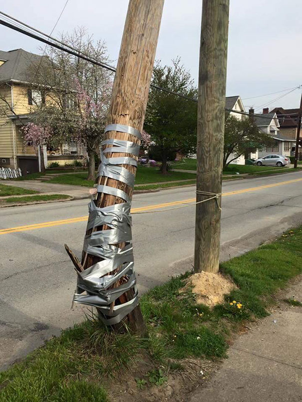 A damaged utility pole poorly repaired with duct tape, showcasing a clear job fail.