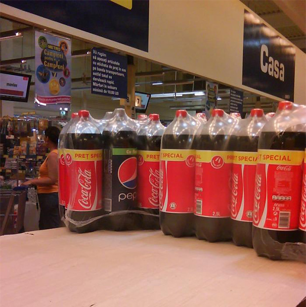 Bottled soda packaging error, with a Pepsi bottle mislabeled as Coca-Cola in a store setting.
