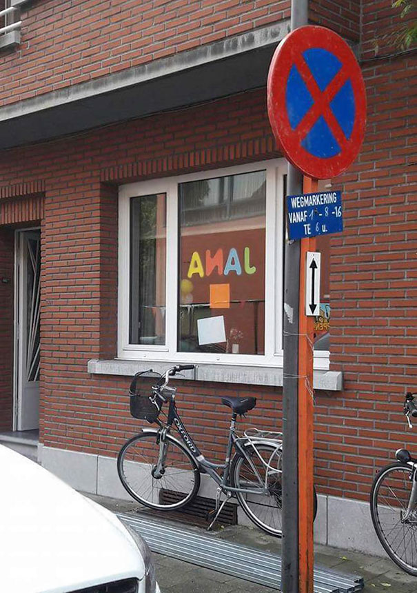 Sign fail with jumbled window letters, bike leaning against a brick wall, and a no parking sign.