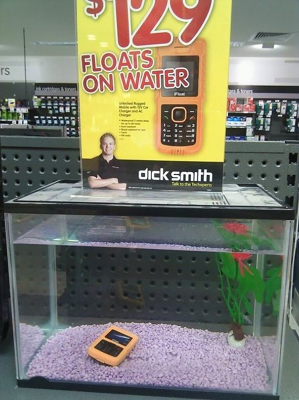 Phone submerged in a fish tank beneath a "floats on water" sign, illustrating a job fail.