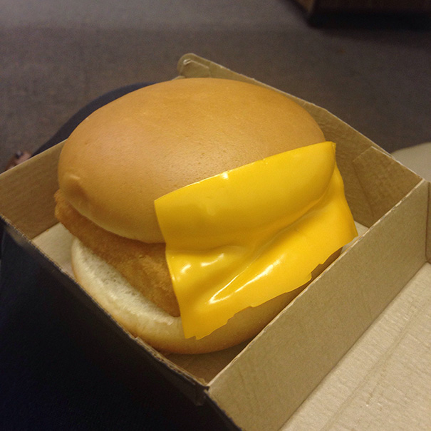 Burger with cheese slice misplaced halfway outside the bun; a humorous example of job failure.