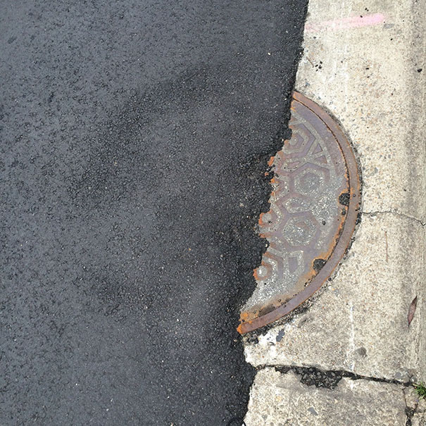 Manhole cover misaligned after road paving, illustrating job failure.