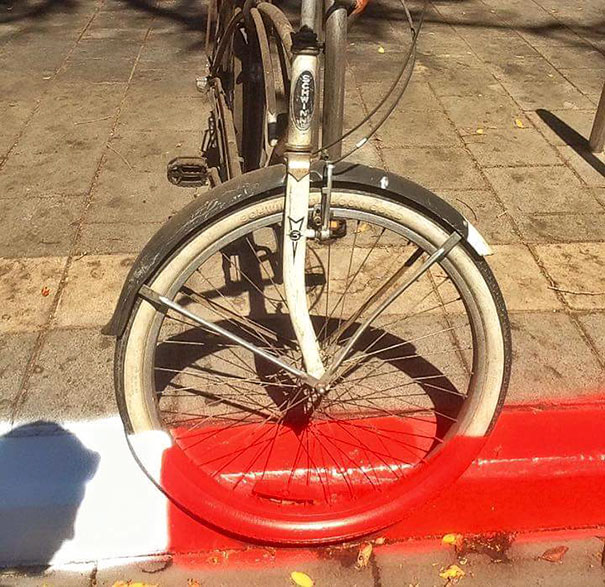 Bicycle parked with a wheel over a freshly painted red curb, highlighting a job fail in a public place.