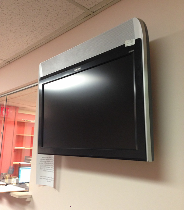 Wall-mounted TV with power button inaccessible, highlighting job fail.