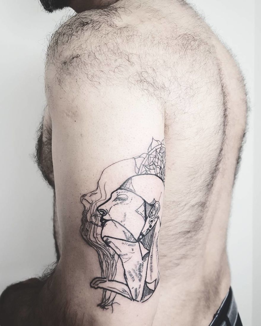 Sketchy tattoo design on a person's upper arm, featuring an abstract face and geometric patterns.