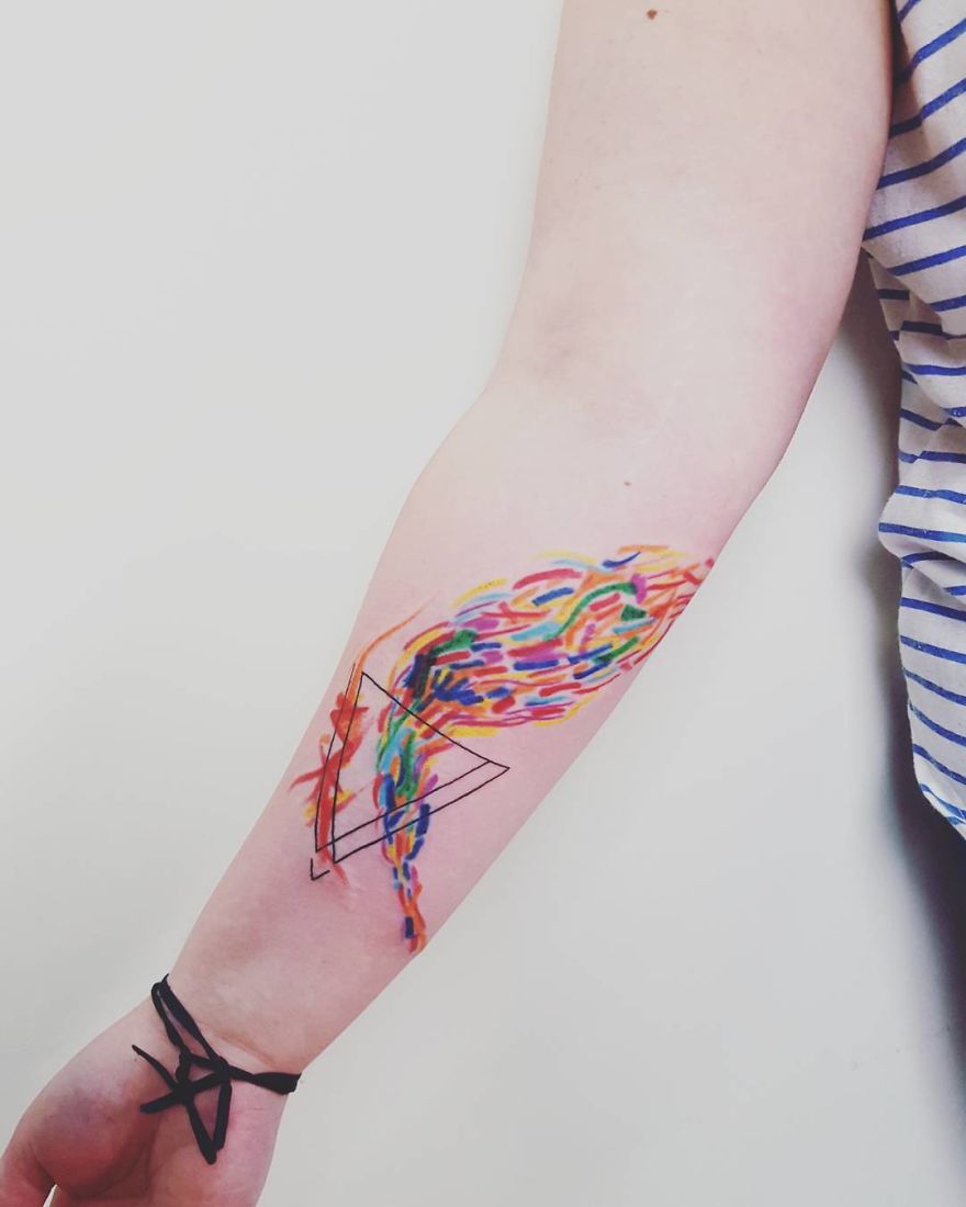 Colorful, sketchy tattoo on forearm featuring vibrant abstract design with geometric shapes.