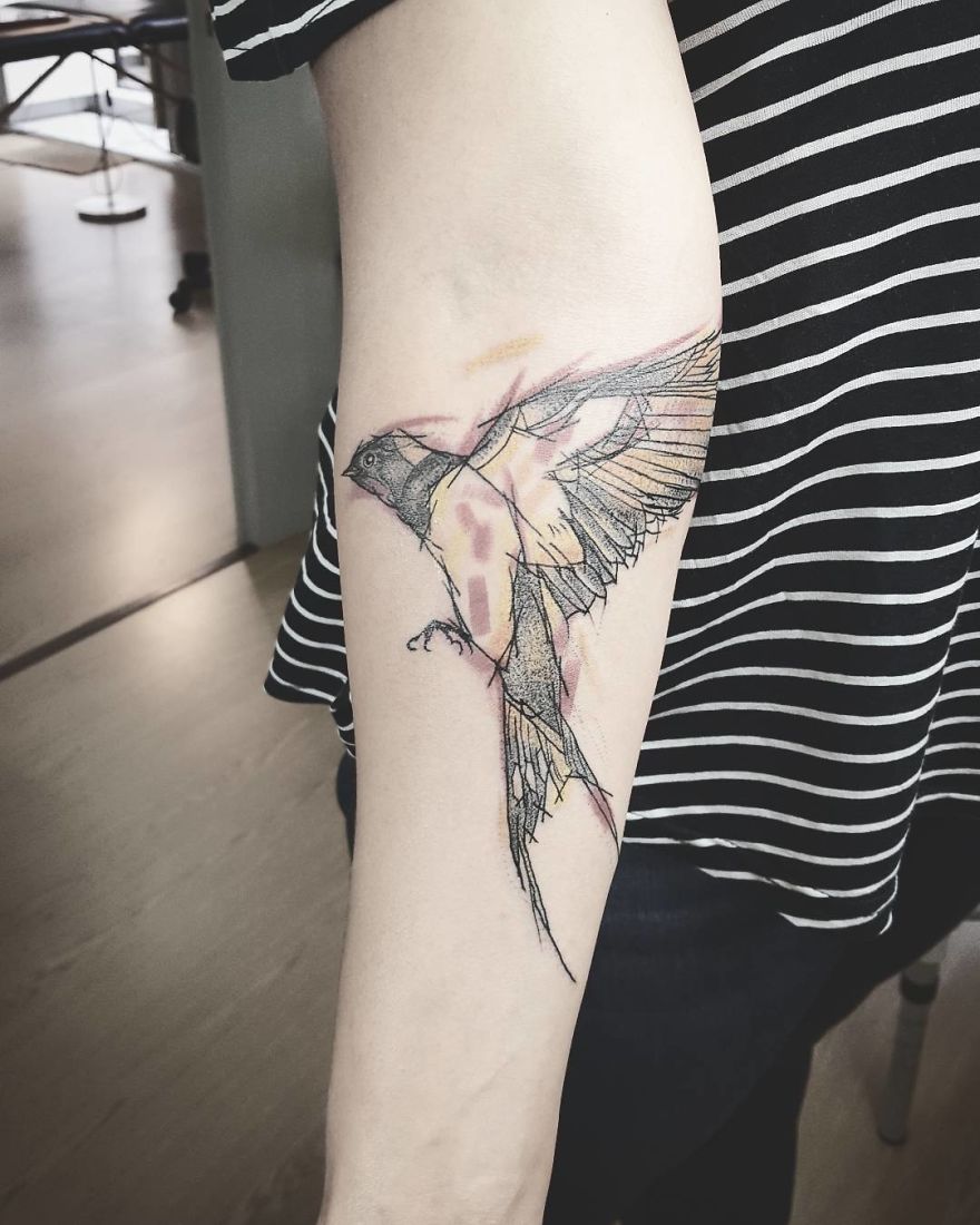 Sketchy tattoo of a colorful bird on a person's arm, showcasing unique design and artistry.
