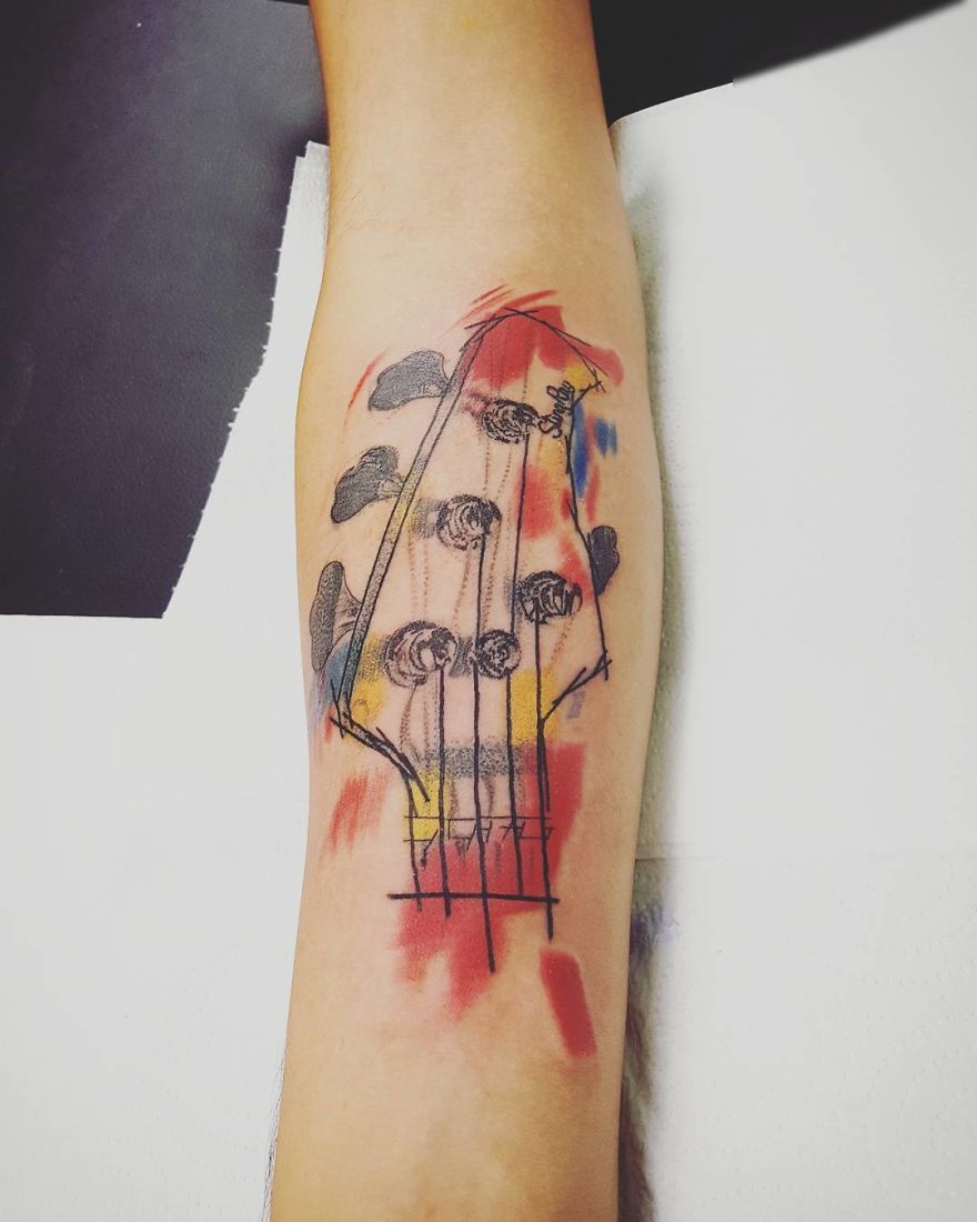 Colorful sketchy tattoo of a guitar head on an arm, featuring vibrant red and yellow splashes.