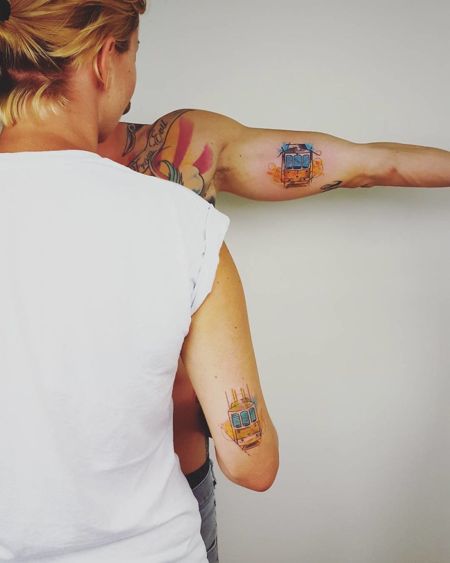 Person displaying colorful, sketchy tattoos on their arm and back, featuring a tram design.
