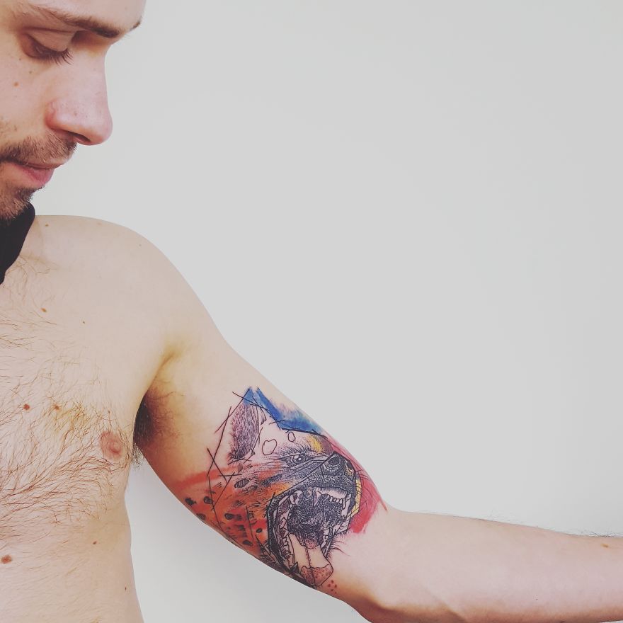 Tattoo with colorful and sketchy style on a man's bicep, featuring a vivid abstract animal design.