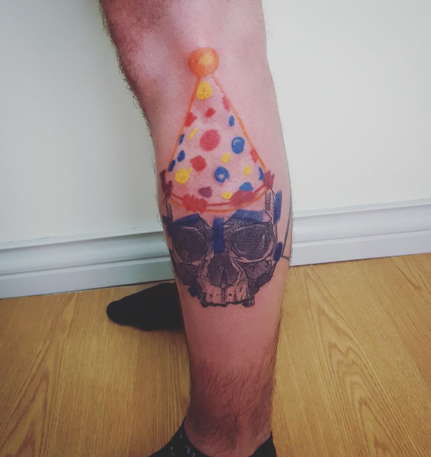 Colorful and sketchy tattoo of a skull wearing a dotted party hat on a person's calf.