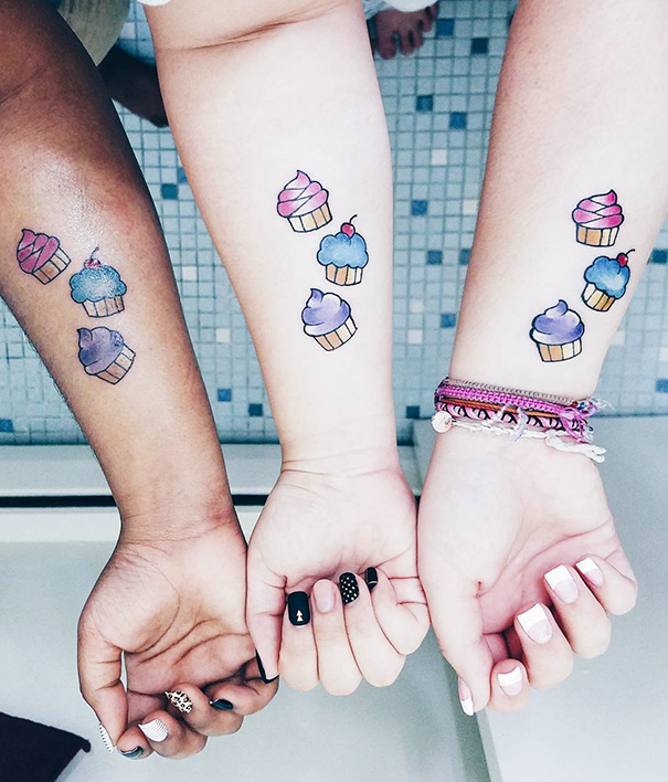 Three forearms with trio tattoos of colorful cupcakes, representing friendship and unity.