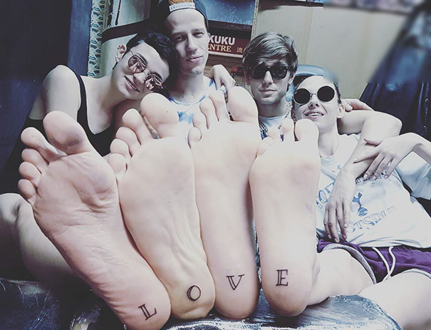 Feet with "LOVE" tattoos, a fun trio tattoo idea, shown with four friends sitting together.