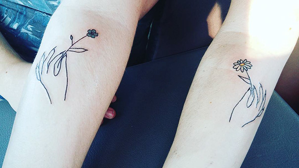 Minimalist trio tattoos of hands holding flowers on arms.
