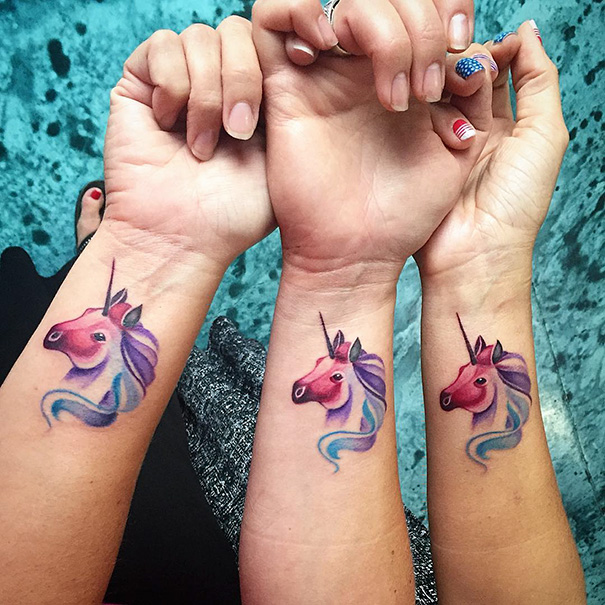 Three wrists with matching unicorn trio tattoos in vibrant colors, symbolizing unity and friendship.