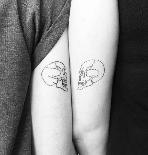 Trio tattoos of skull outlines on two arms, facing each other.
