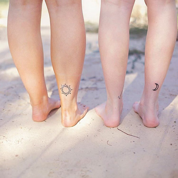 Three legs with trio tattoos: sun, small moon, and a minimalist design, standing on sandy ground.