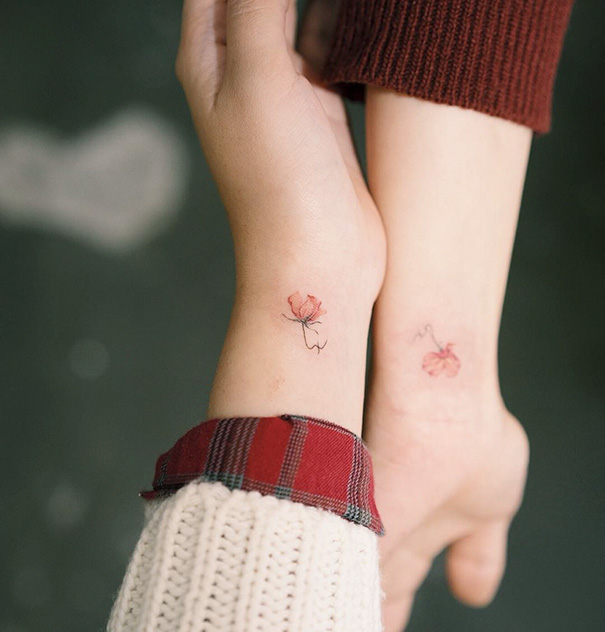 Minimalist trio tattoos of flowers on wrists, with one wrist in a red plaid sleeve.