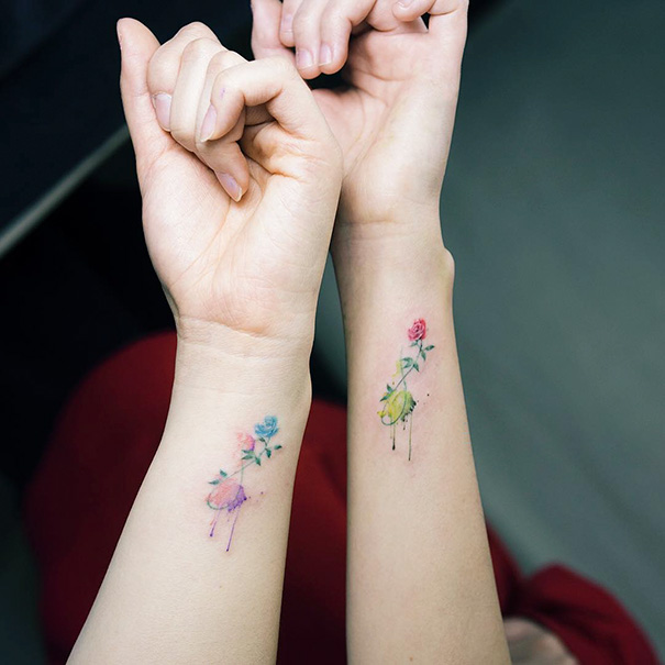 Minimalist trio tattoos of flowers on intertwined wrists, showcasing vibrant colors and delicate designs.