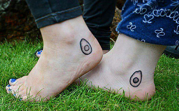 Two feet with matching avocado tattoos, showcasing trio tattoo ideas on grass background.
