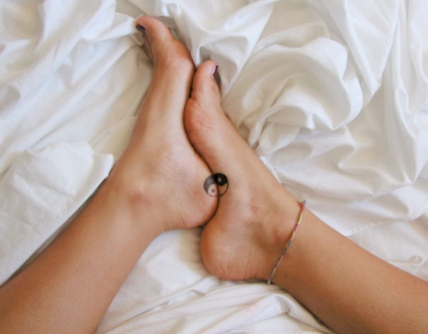 Feet with matching yin-yang tattoos, representing a trio tattoo idea, lying on a white sheet.