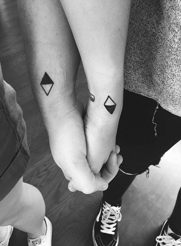 Close-up of two hands with geometric trio tattoos, depicting simple diamond shapes in black ink.