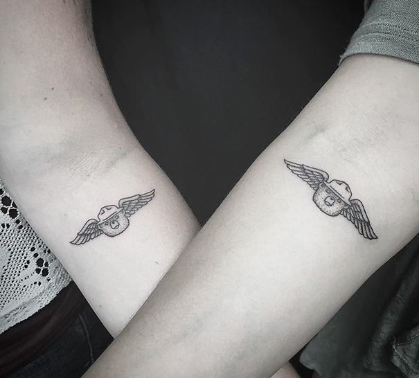 Matching winged helmet trio tattoos on two forearms, symbolizing unity in a creative design.