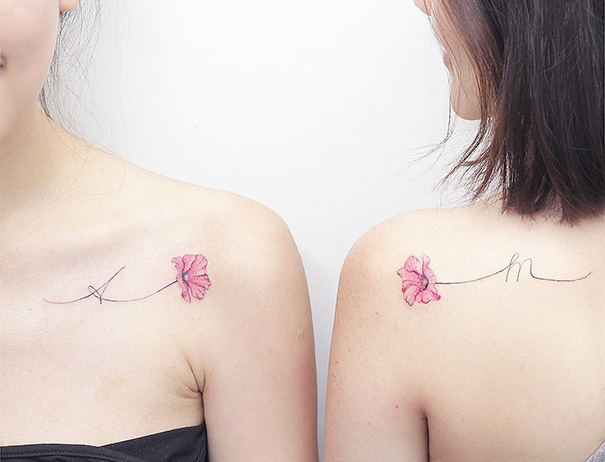 Two women with matching pink flower trio tattoos on their shoulders, symbolizing unity and friendship.