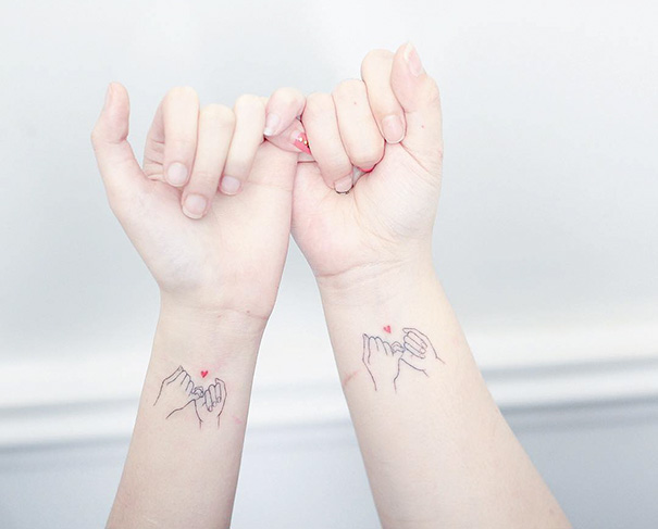 Minimalist trio tattoos of linked hands on wrists, featuring small red hearts above each design.
