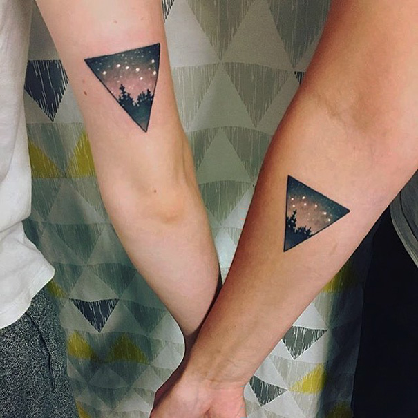 Two matching triangle tattoos on forearms, showcasing a night sky design.