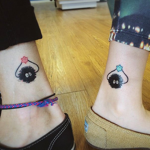 Unique trio tattoos on ankles, featuring soot sprite designs with colorful stars, on a wooden floor background.