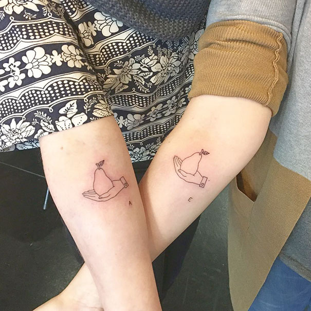 Matching trio tattoos of hands holding pears on two arms.