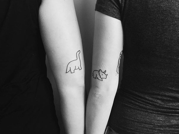 Minimalist trio tattoos featuring dinosaur and rhino designs on two people's arms.