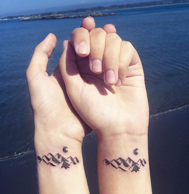 Minimalist trio tattoos of mountains and a crescent moon on wrists by the ocean.