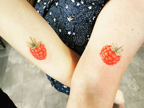 Trio tattoos featuring matching raspberry designs on two forearms.