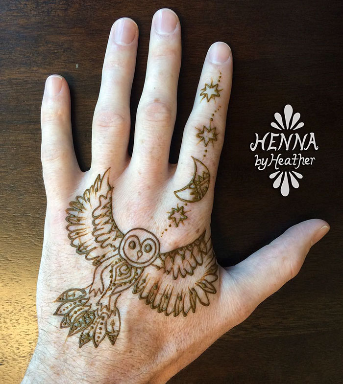 Intricate henna tattoo of an owl and celestial symbols on a man's hand.