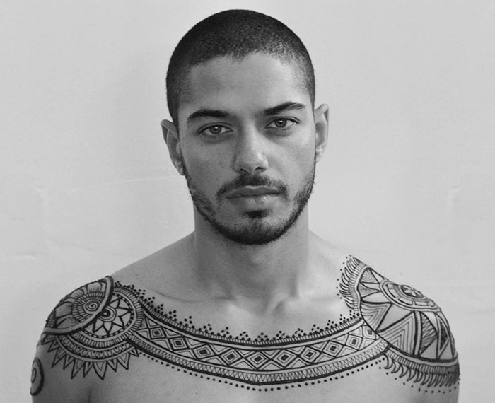 Man with intricate henna tattoos across shoulders and chest, showcasing the Menna trend in body art.