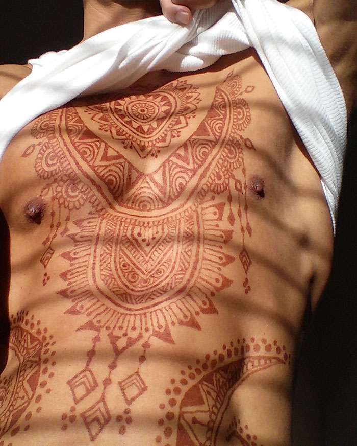 Man displaying intricate henna tattoos on his chest, highlighting the 'Menna' trend in body art.