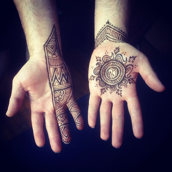 Men's hands featuring intricate Menna designs with detailed henna tattoos on palms and fingers.