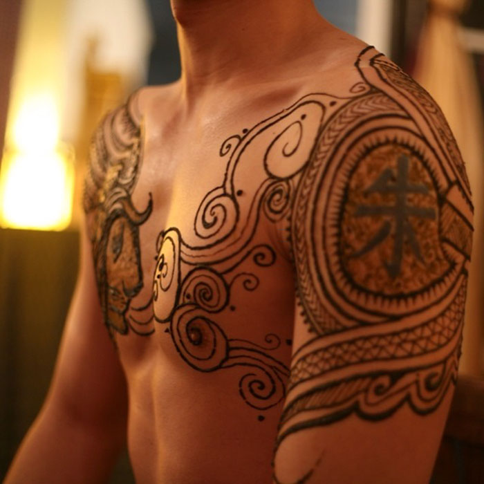Man with intricate henna tattoos on chest and arms, showcasing the 'Menna' trend.