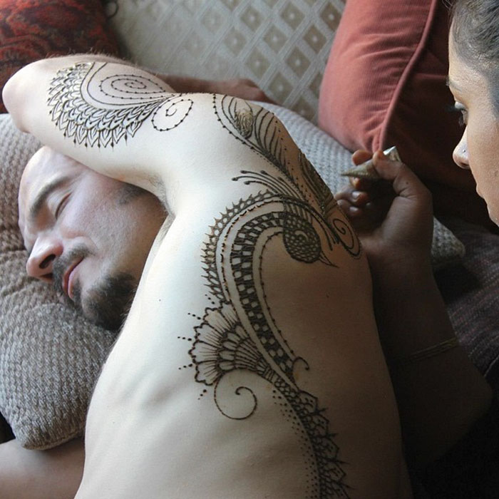 Man with intricate henna tattoo art on arm, showcasing the 'Menna' trend in a relaxed setting.