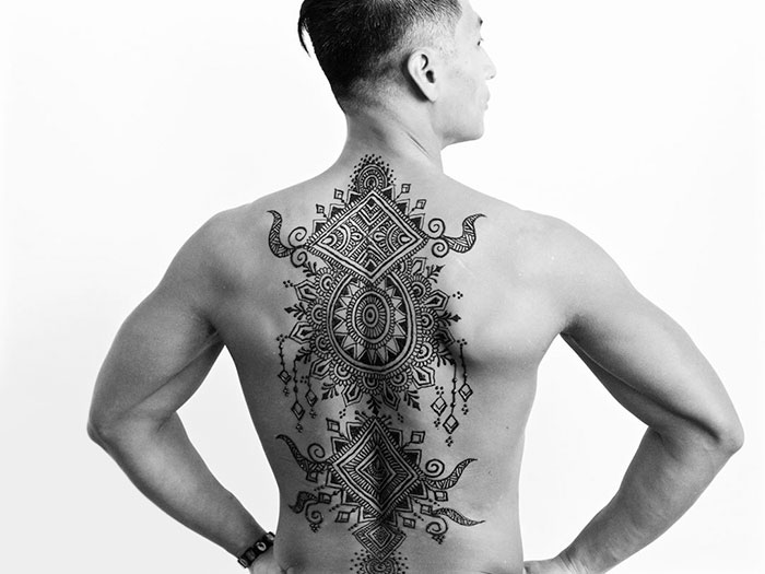 Man with intricate henna tattoos on back, showcasing 'Menna' trend fashion for men.