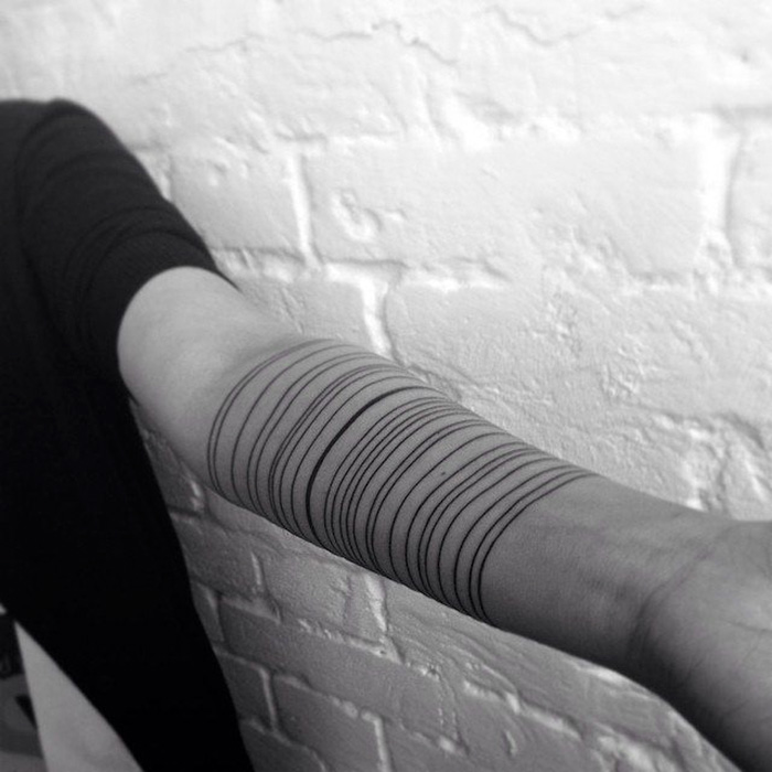 Minimalist digitally-designed tattoo of concentric circles on an arm against a white brick wall.