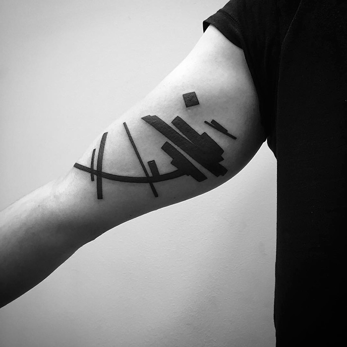 Minimalist digitally-designed tattoo on a person's forearm with abstract black lines and shapes.